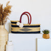 Woven basket with red handles on a white surface with decorative items.