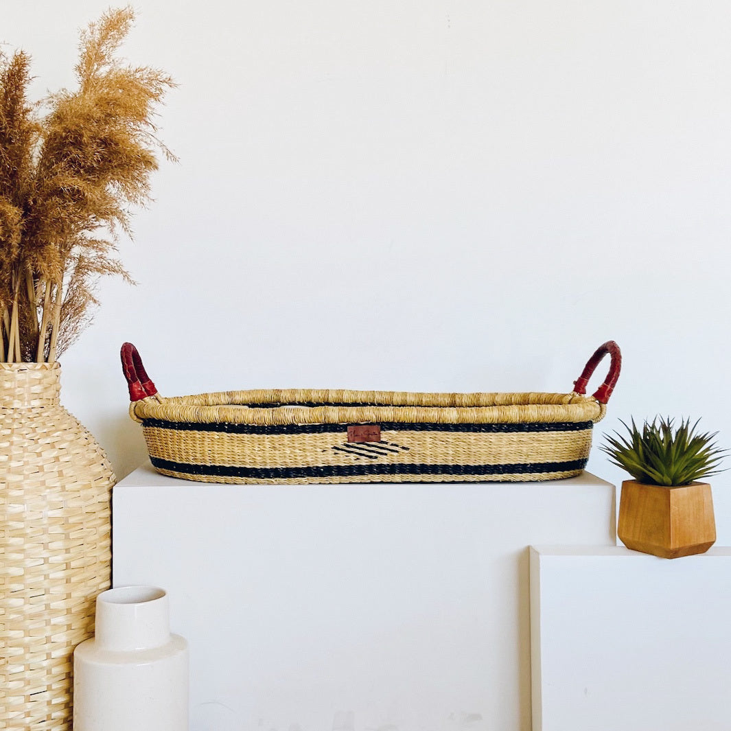 Meadow Changing Basket handwoven from elephant grass with navy plant-based dye, made in Ghana, shown with included mattress