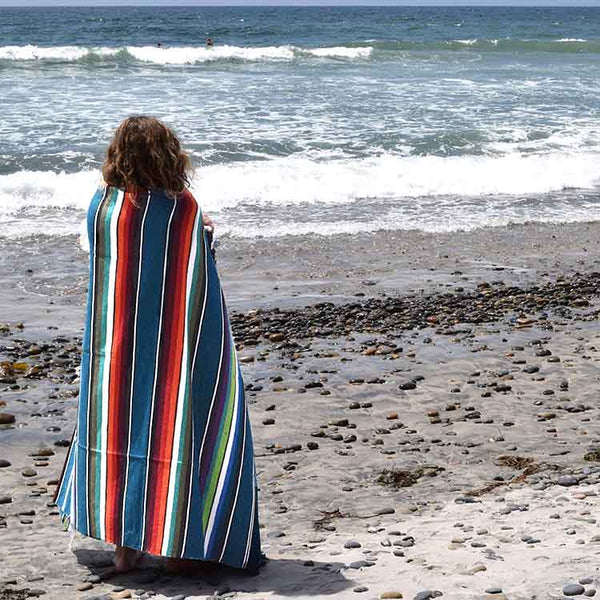 Person standing on a beach with a colorful striped towel draped over them