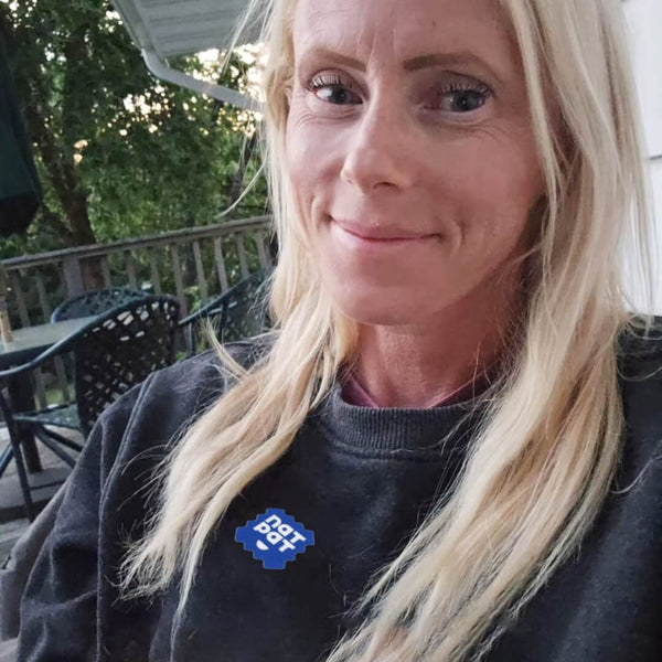 Woman with blonde hair wearing a dark sweatshirt with a logo outdoors.