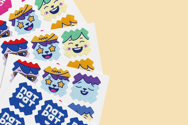 Sheet of colorful stickers with cartoon faces and 'nat pat' branding on a beige background. NATPAT kids mosquito patches — DEET-free, plant-based citronella & eucalyptus protection for babies & children. Up to 8 hours. No skin contact. Perfect family gift.