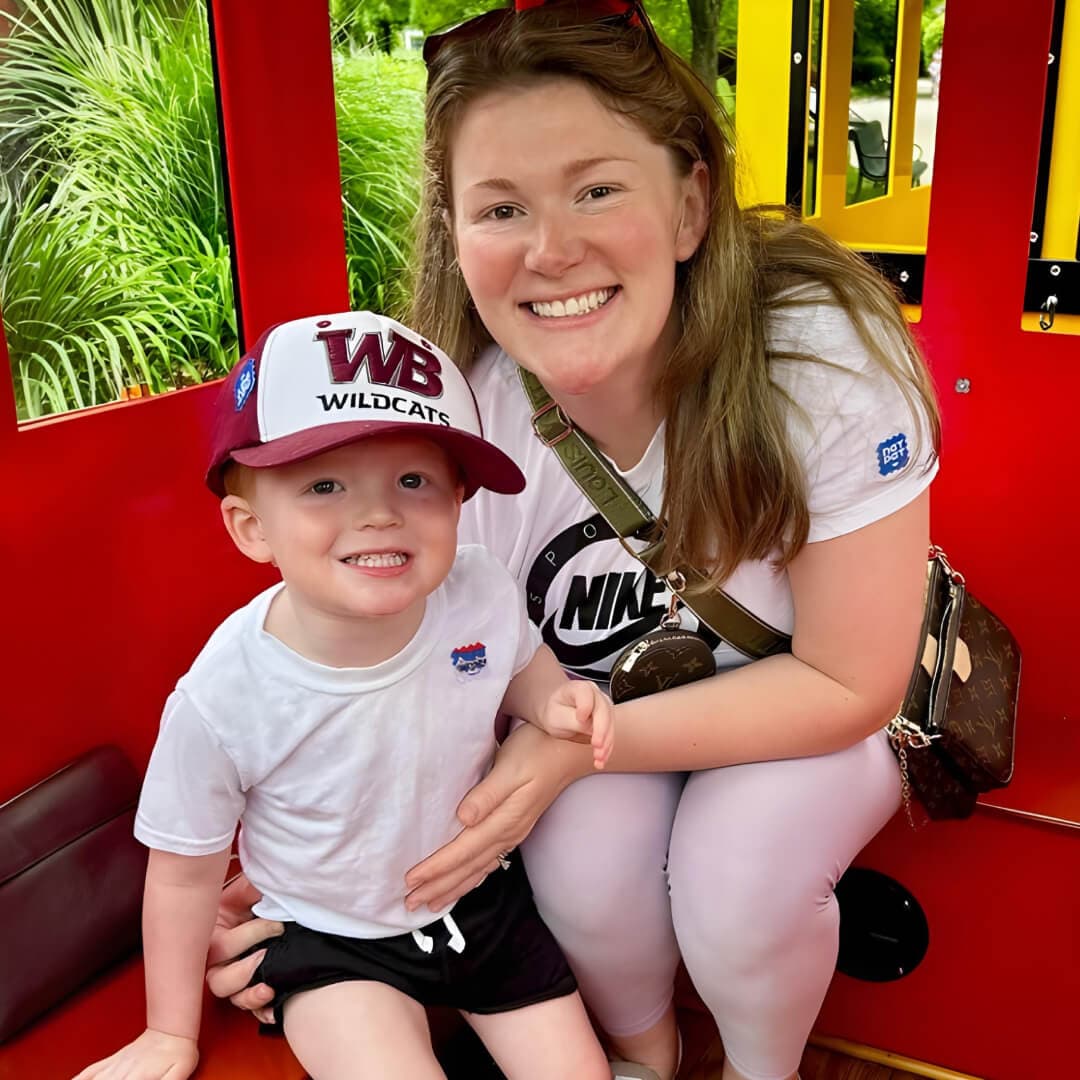Woman and child sitting on a red train, both wearing white shirts with logos.