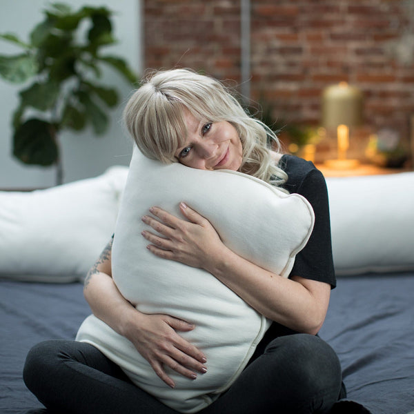 Woman hugging a large white pillow in a cozy room with a brick wall and plants.