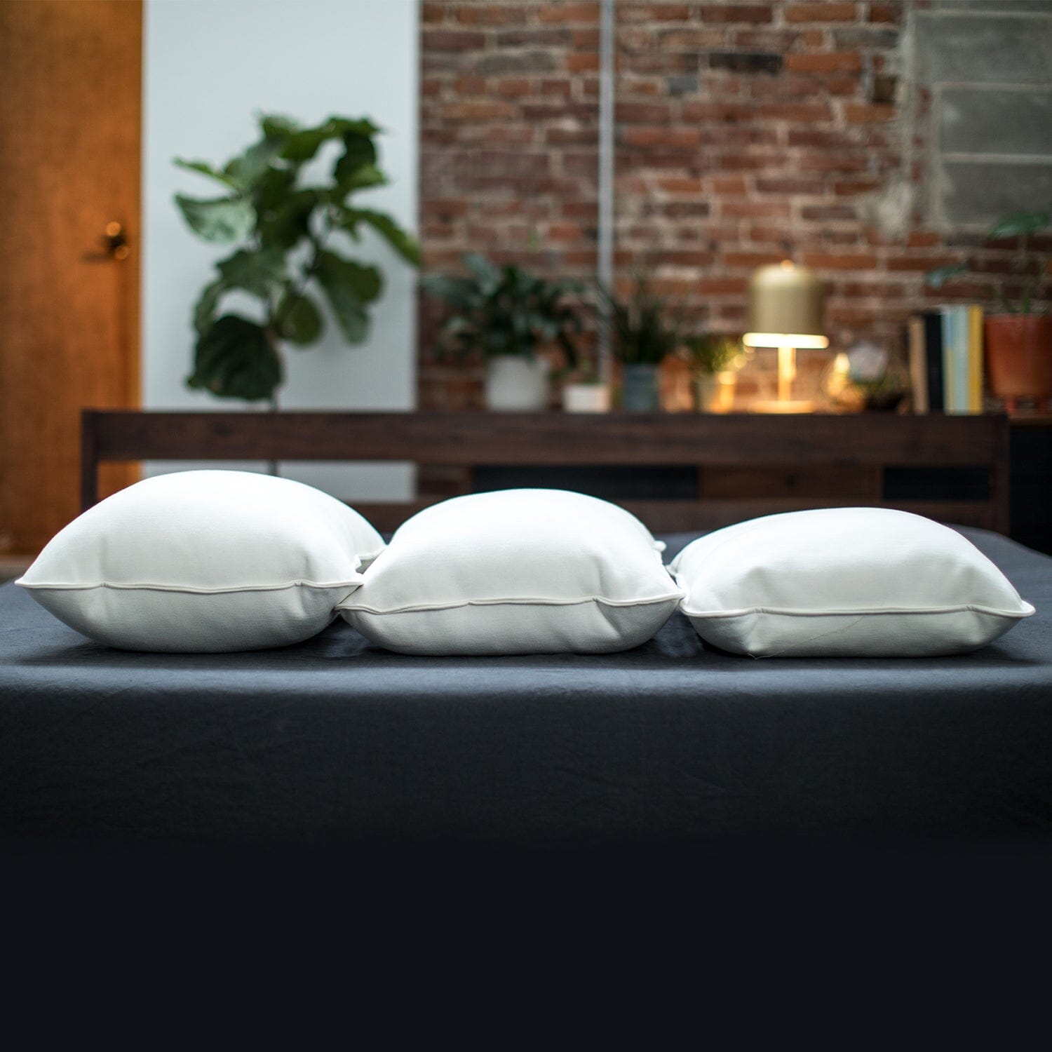 Three white pillows on a bed with a rustic room background