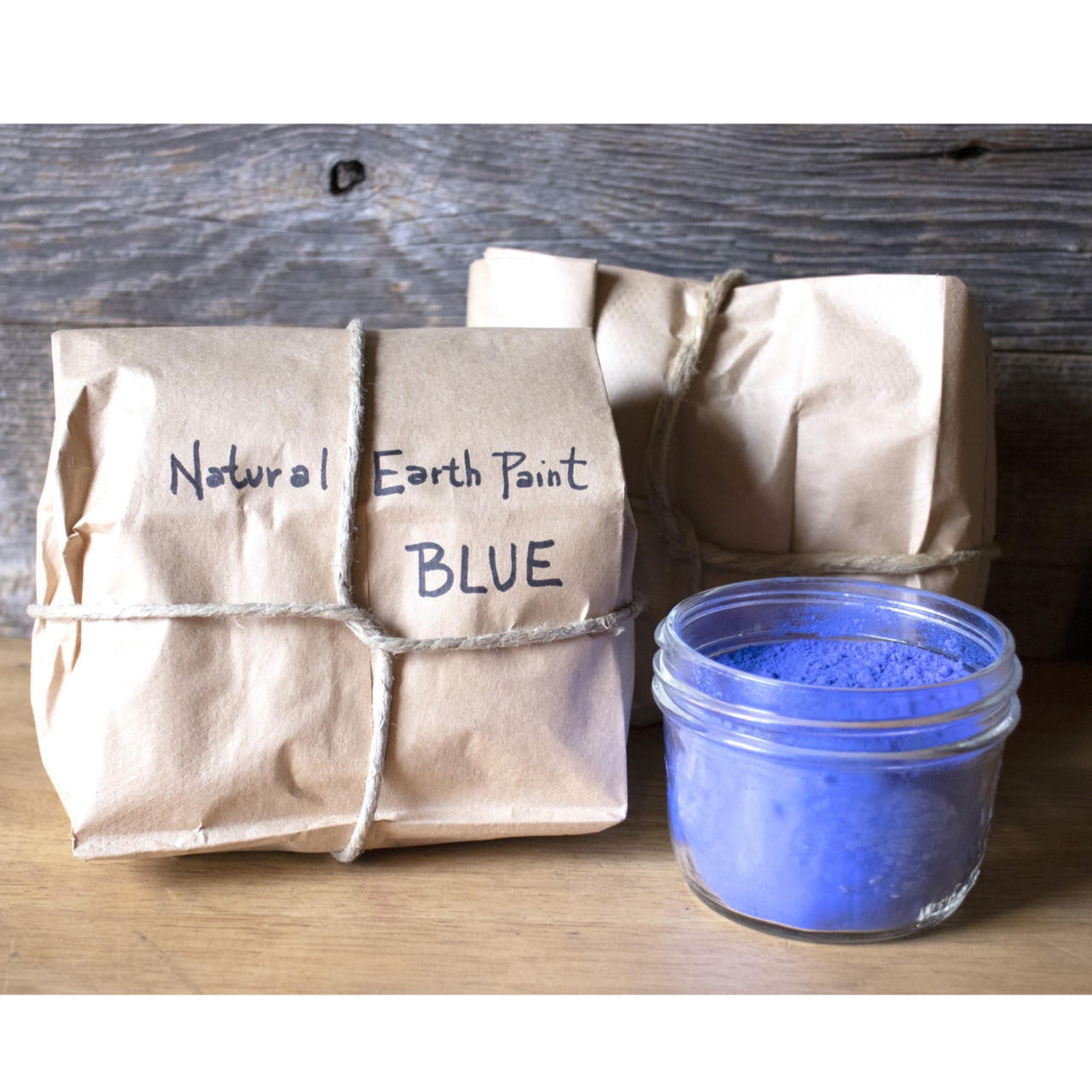 Jar of blue natural earth paint next to a brown paper bag labeled 'Natural Earth Paint Blue'.