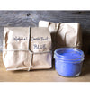 Jar of blue natural earth paint next to a brown paper bag labeled 'Natural Earth Paint Blue'.