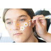 Person applying white flowers with yellow centers to a person's face using a brush.