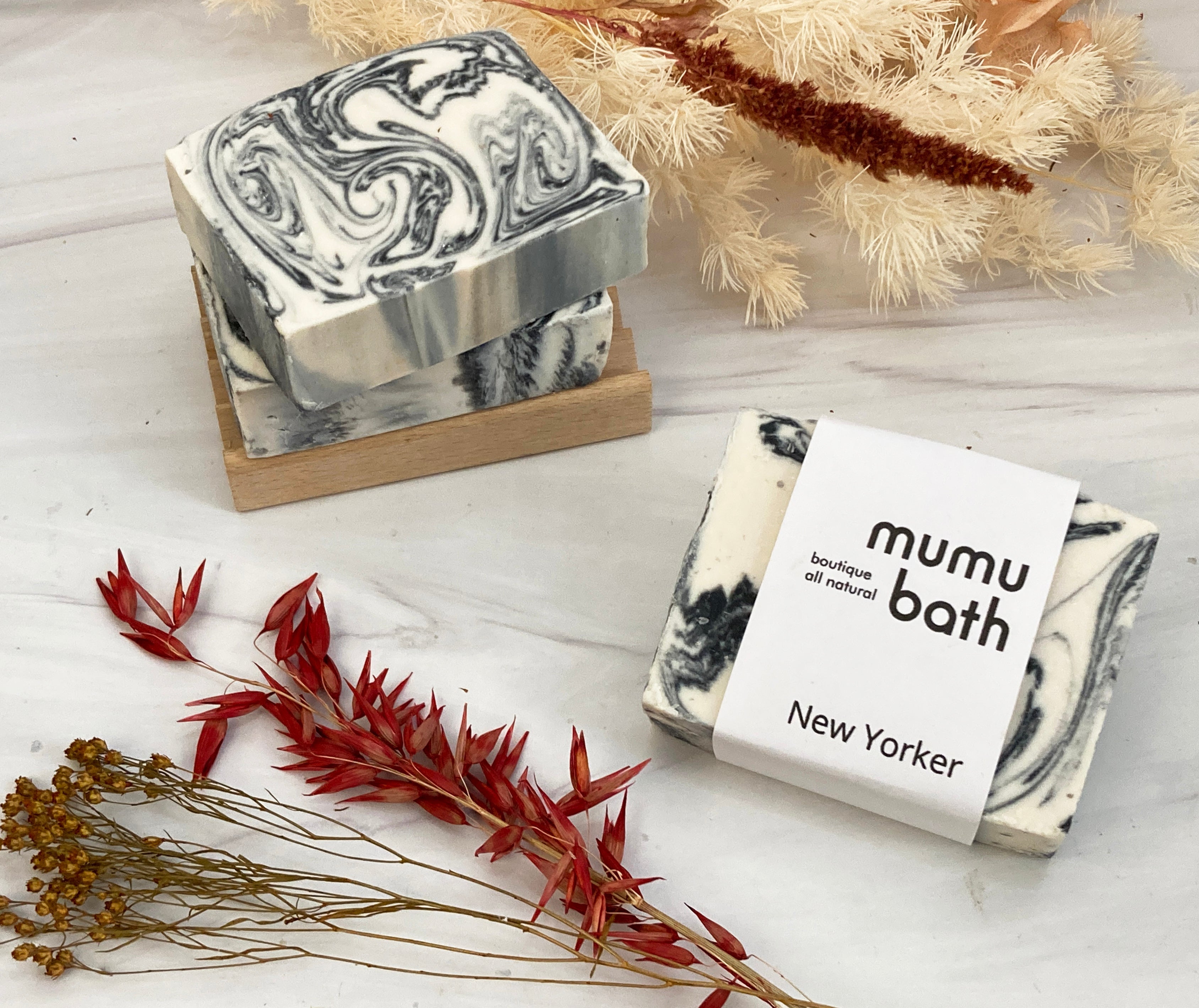 A close-up of the soap bar, showing the black and white color and the Mumu Bath logo.