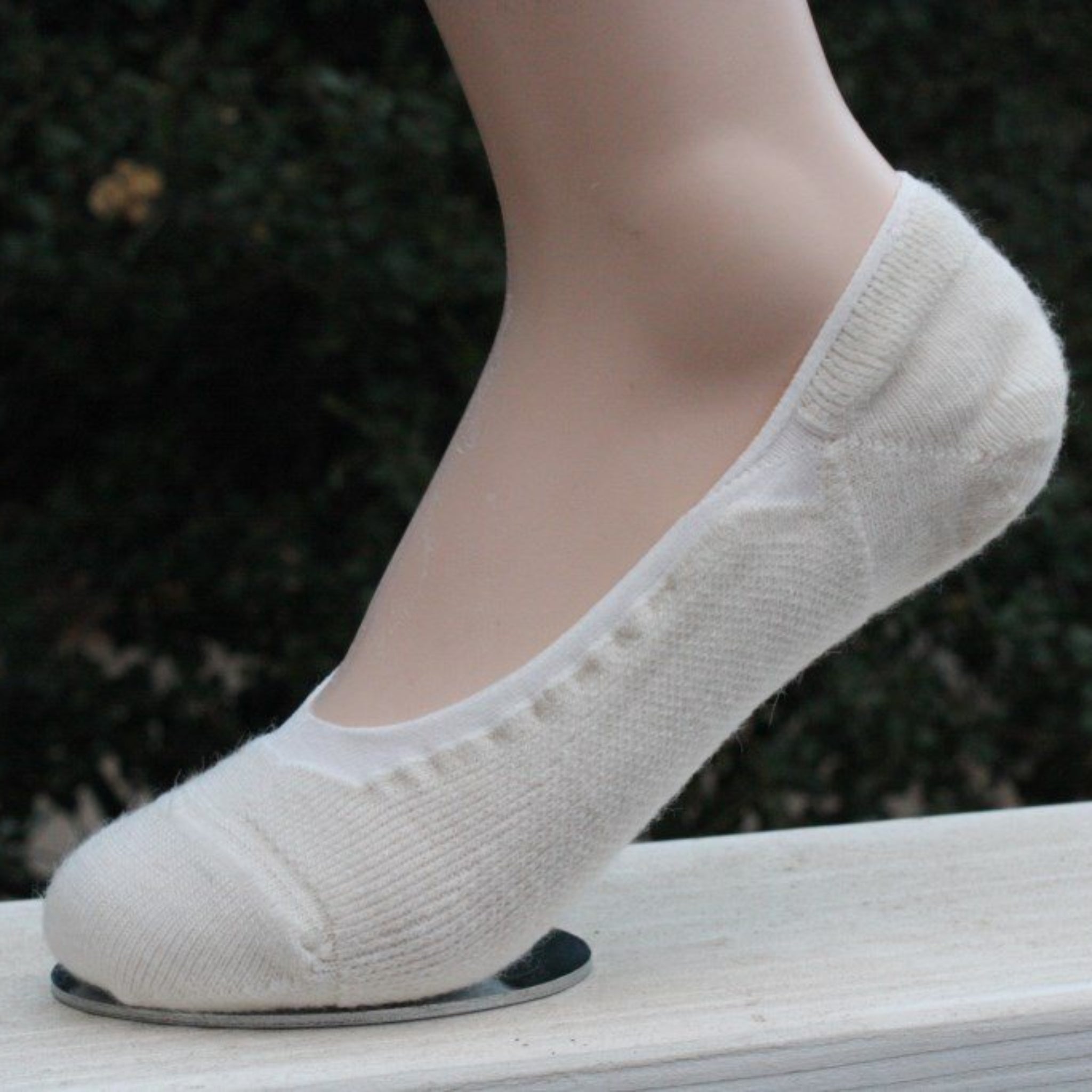 White socks worn by a person standing on a wooden surface with a blurred natural background