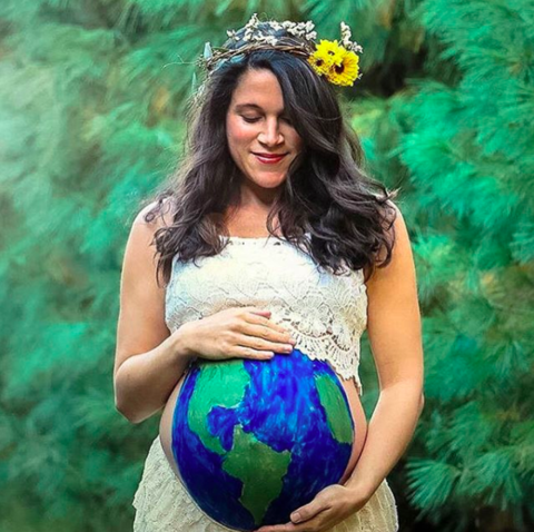 Pregnant woman holding a globe-shaped balloon with a green and blue design, surrounded by greenery.