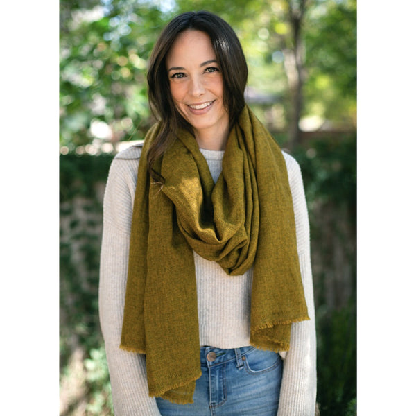 Woman wearing a green cashmere scarf outdoors with blurred greenery in the background