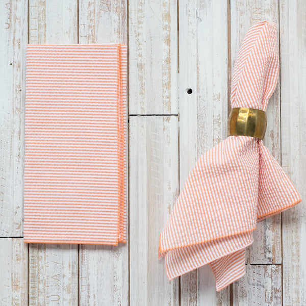 Pink striped napkin with a gold napkin ring on a wooden surface