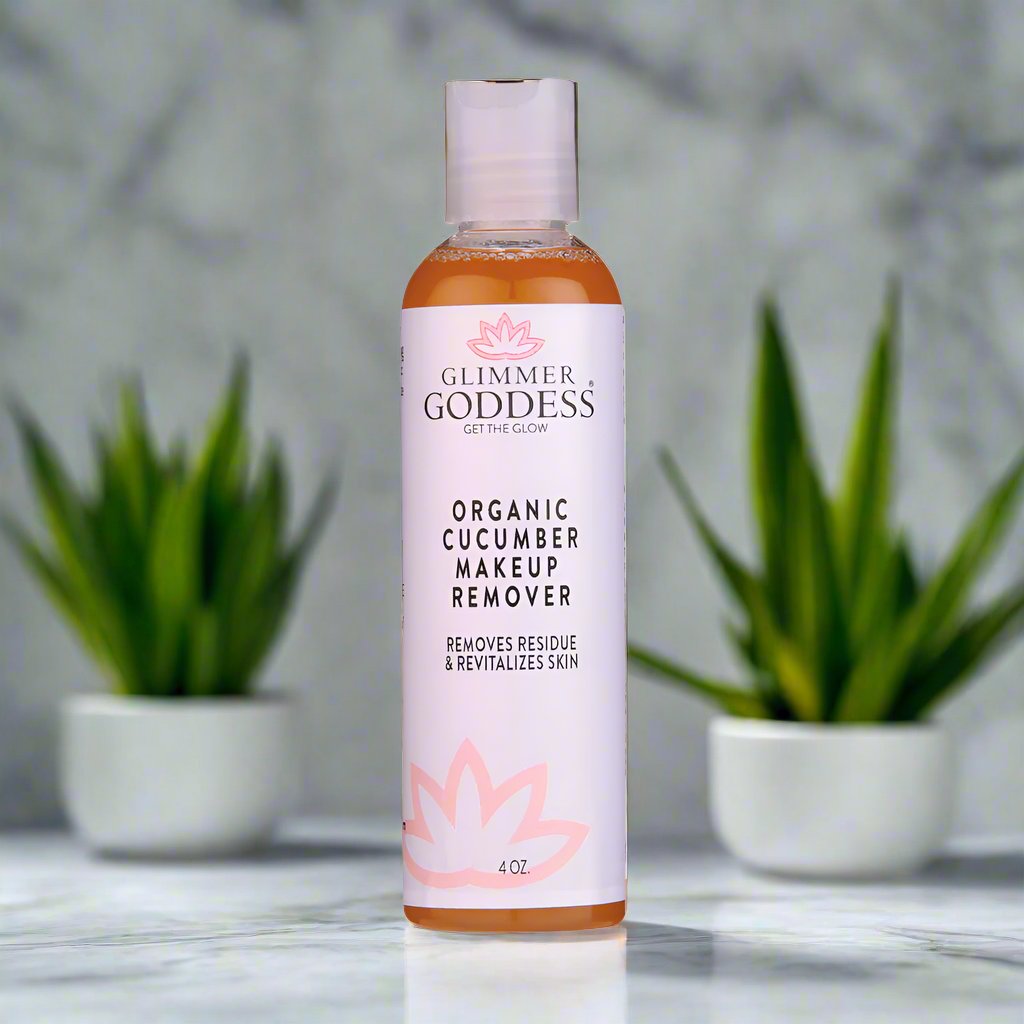 Bottle of Glimmer Goddess Organic Cucumber Makeup Remover on a marble surface with plants in the background.