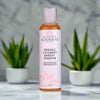 Bottle of Glimmer Goddess Organic Cucumber Makeup Remover on a marble surface with plants in the background.