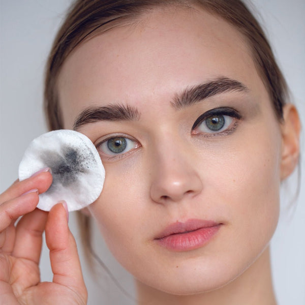 Woman holding a cotton pad with blackhead removal product against a neutral background