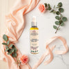 Glimmer Goddess Organic Nourishing Body Oil bottle with flowers and ribbons on a marble surface