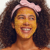 Woman with a yellow facial mask on her face, wearing a pink headband.