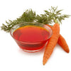 Glass bowl of carrot juice with fresh carrots and carrot tops on a white background