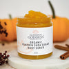 Organic pumpkin body scrub jar surrounded by autumn ingredients including pumpkin and shea butter
