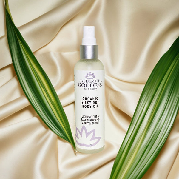 Bottle of Glimmer Goddess organic silky dry body oil on a beige fabric background with green leaves.