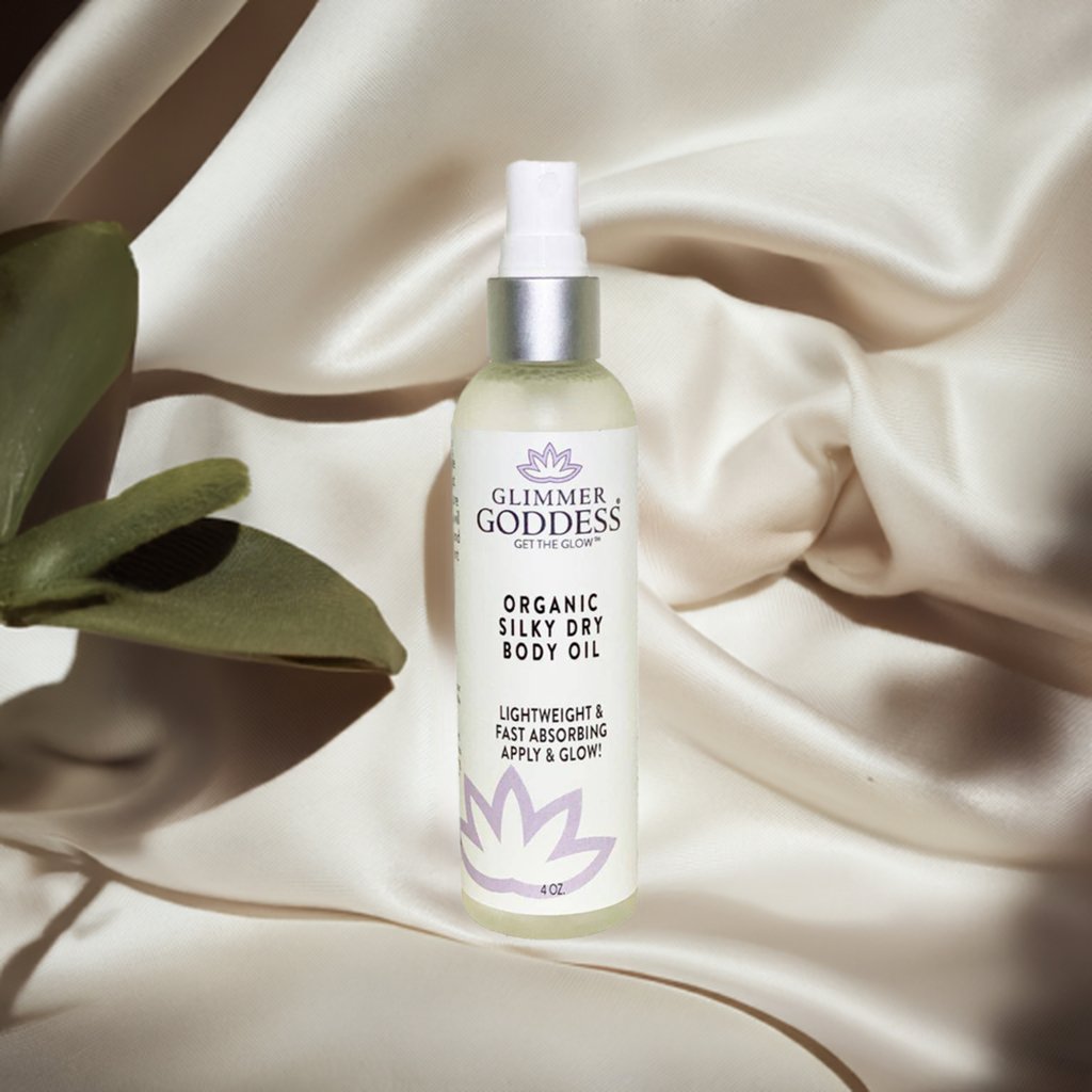 Glimmer Goddess organic silky dry body oil bottle on a beige fabric background with a leaf.
