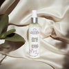 Glimmer Goddess organic silky dry body oil bottle on a beige fabric background with a leaf.