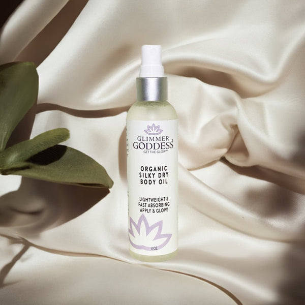 Glimmer Goddess organic silky dry body oil bottle on a beige fabric background with a leaf.
