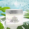 Glimmer Goddess organic whipped body butter jar with green leaves in the background
