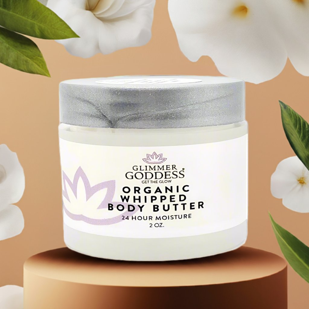 Jar of Glimmer Goddess Organic Whipped Body Butter on a brown background with flowers.