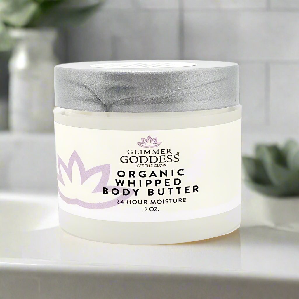 Jar of Glimmer Goddess Organic Whipped Body Butter on a bathroom counter with plants in the background.