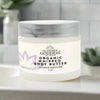 Jar of Glimmer Goddess Organic Whipped Body Butter on a bathroom counter with plants in the background.