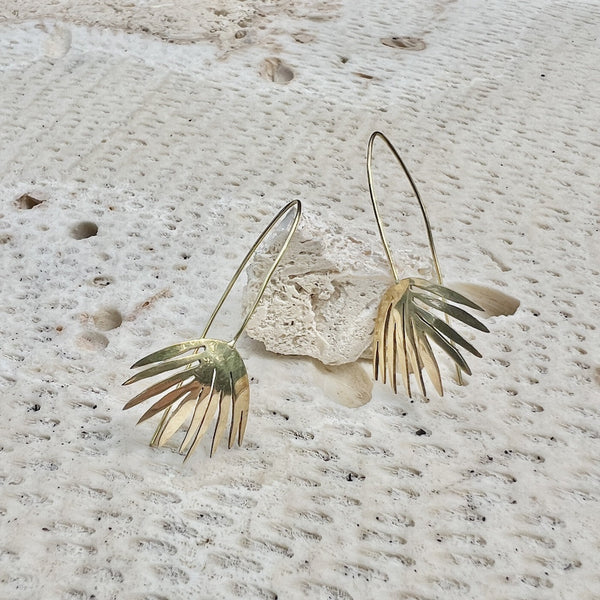 Gold leaf-shaped earrings on a textured stone surface