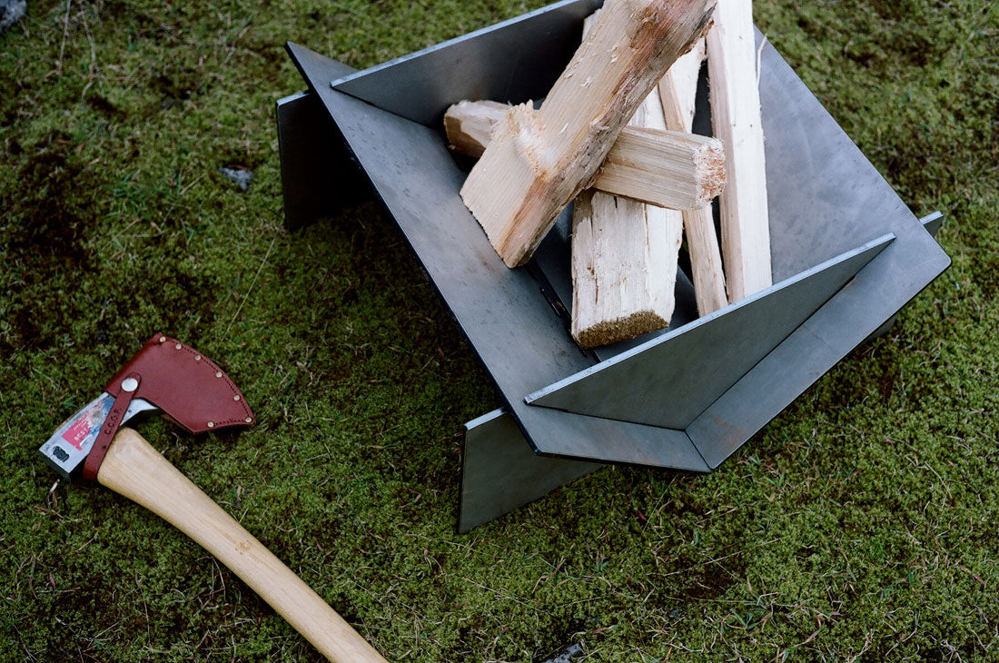 Metal fire pit with wood and axe on grass
