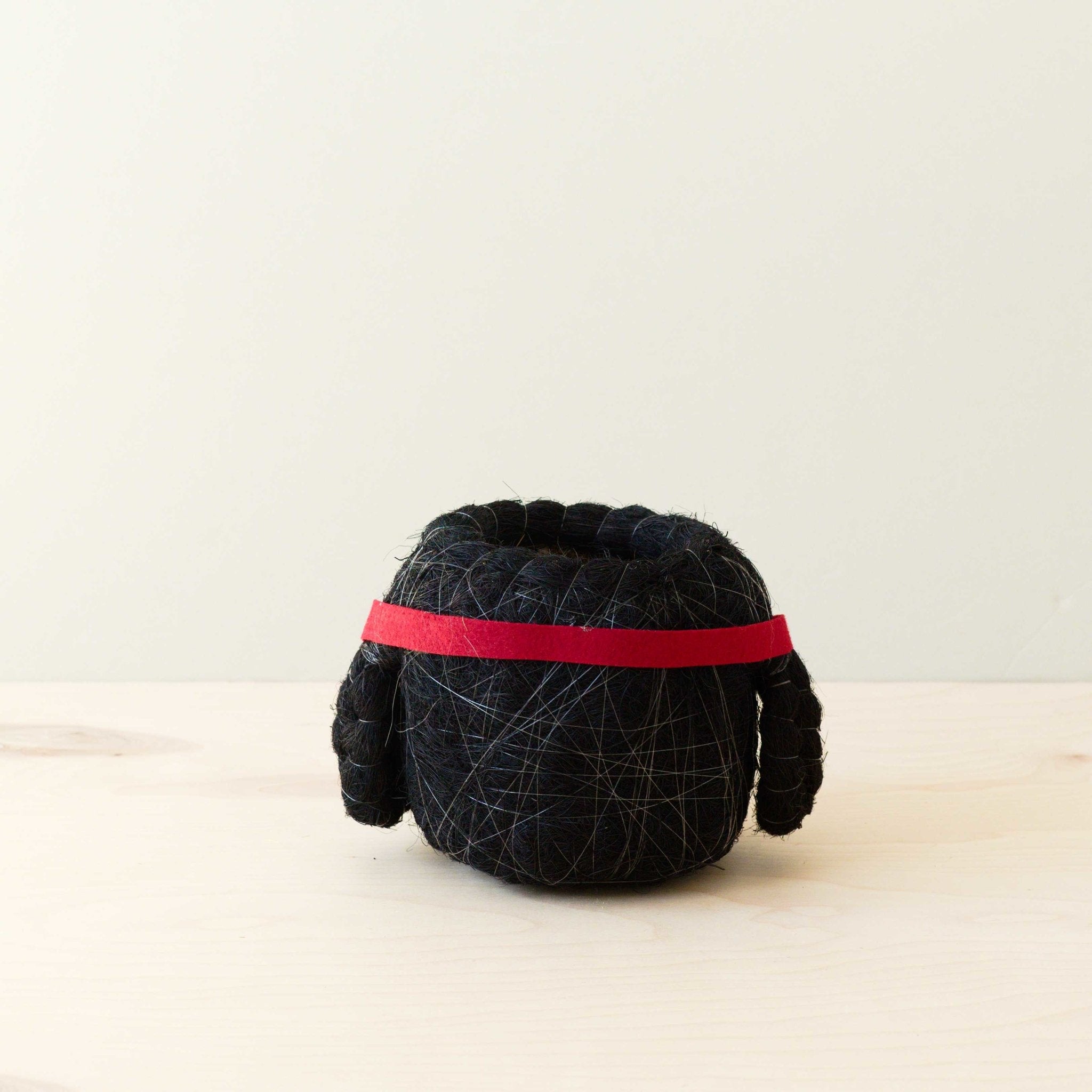 Black yarn ball with a red band on a light beige background