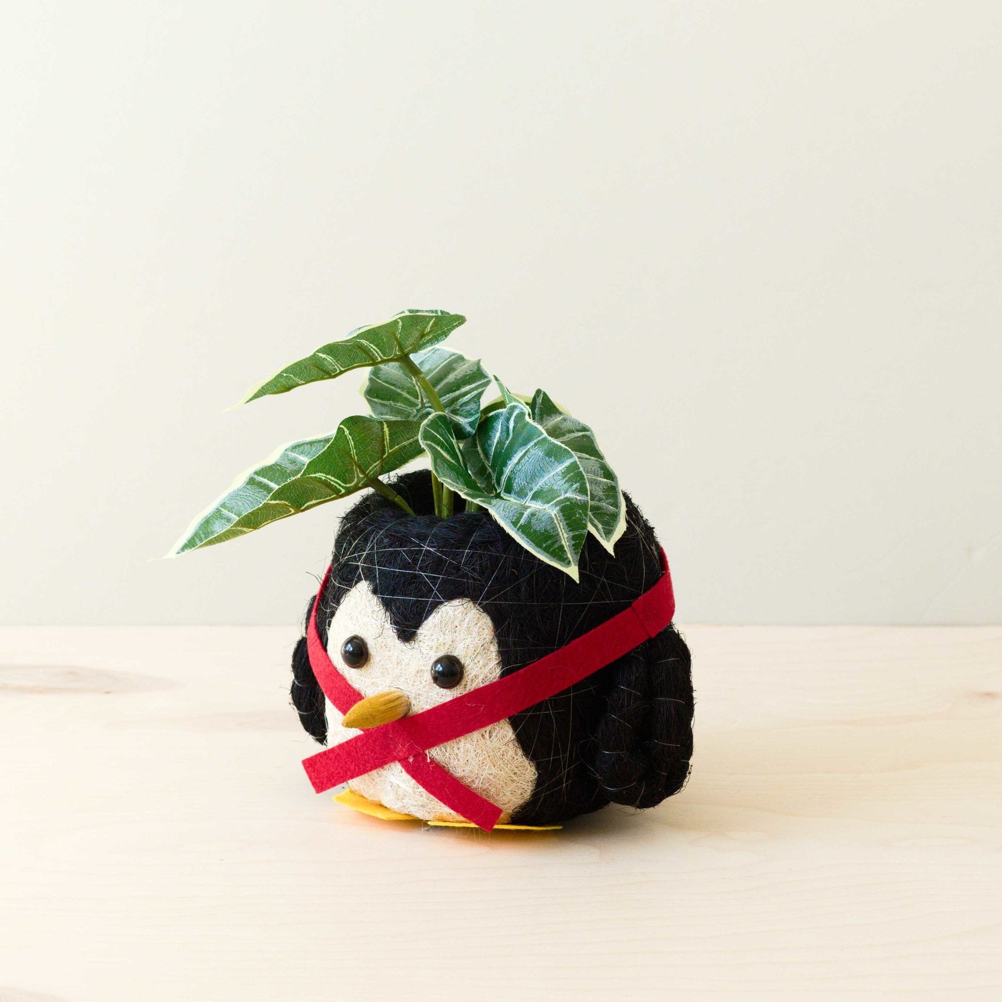 Plush toy penguin with a red ribbon and green leaf on a light background