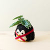 Plush toy penguin with a red ribbon and green leaf on a light background