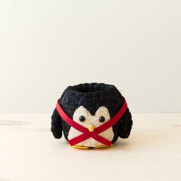 Small plush penguin toy with a red harness on a light background