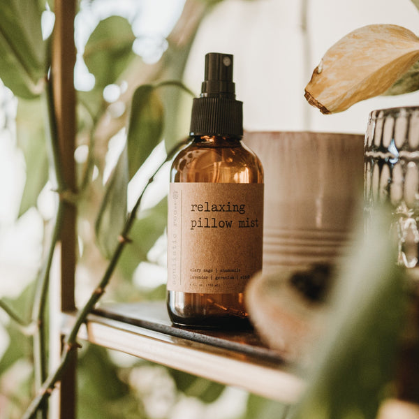 A bottle of Relaxing Pillow Mist spray placed on a bed next to a cushion, with a soft, warm-toned backdrop.