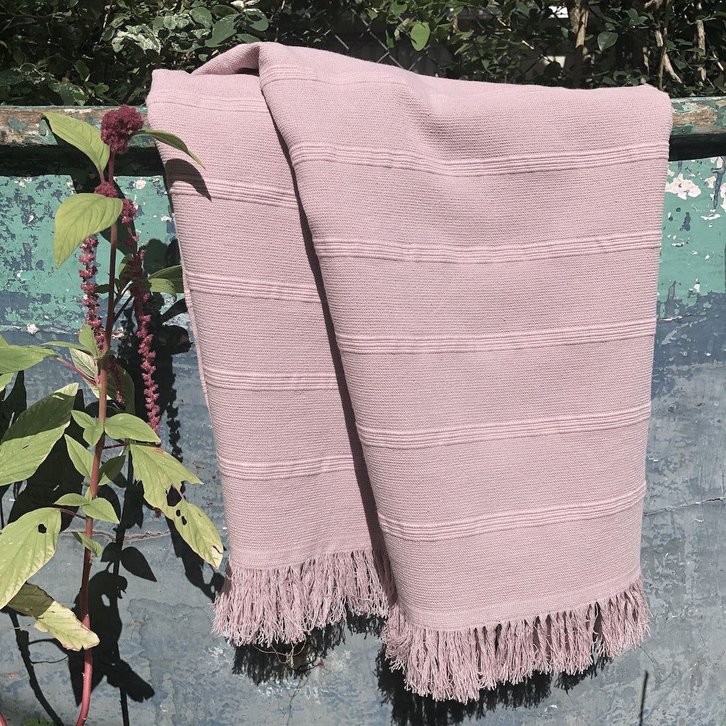 Pink towel with fringes draped over a fence with greenery in the background