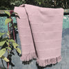 Pink towel with fringes draped over a fence with greenery in the background