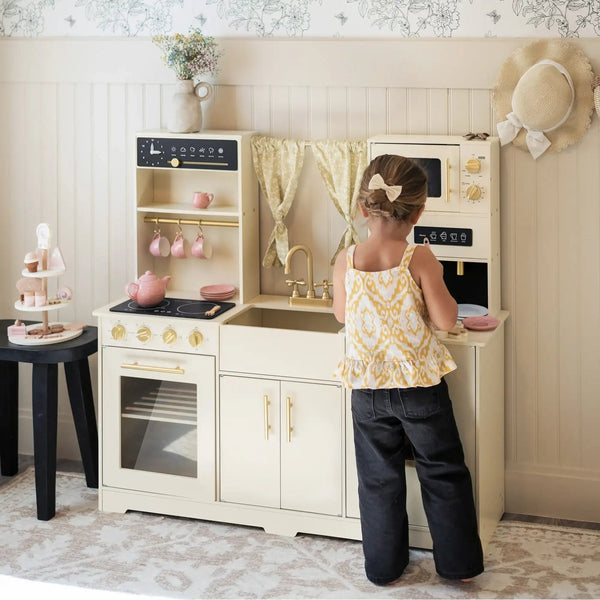 Young child playing with the Tiny Land wooden toy kitchen set featuring oven, microwave and storage