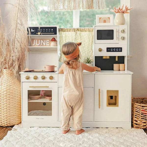 Child using the Tiny Land cream pretend play kitchen in a bright, naturally lit playroom