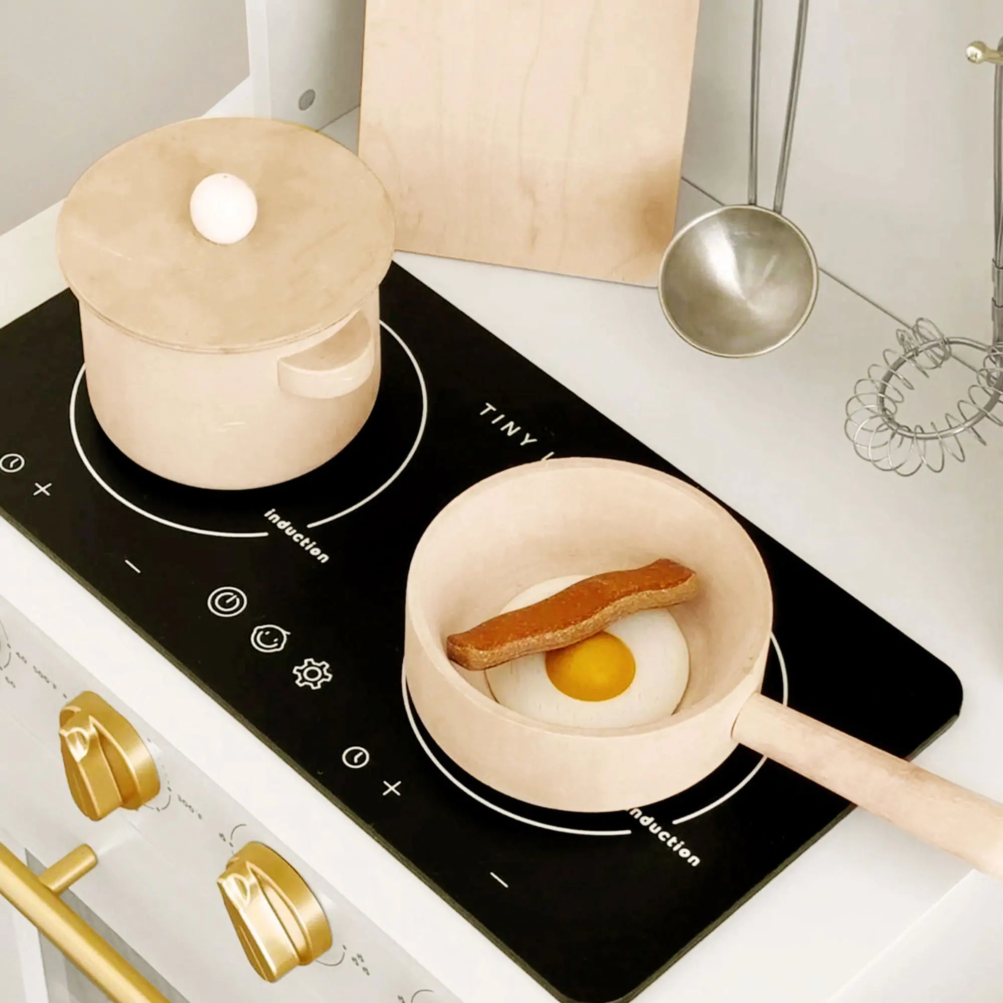 Miniature frying pan with food on a toy stove, featuring the brand 'TINY'.