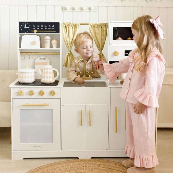 Two children playing with a toy kitchen set in a room.