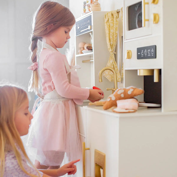 Two young girls playing with a toy kitchen set.