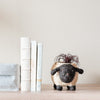Sheep-shaped plant pot with a small plant on a wooden surface next to books.