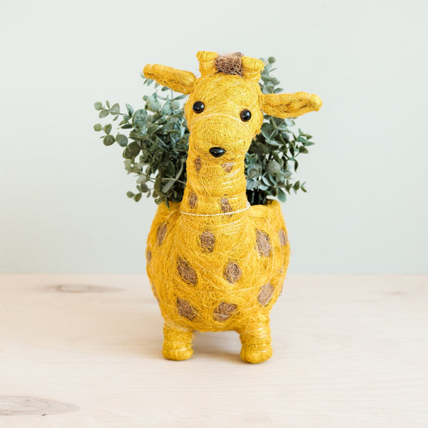 Yellow giraffe-shaped planter with a plant on a light background