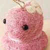 Pink yarn sculpture shaped like a bear with a white bow on a beige background