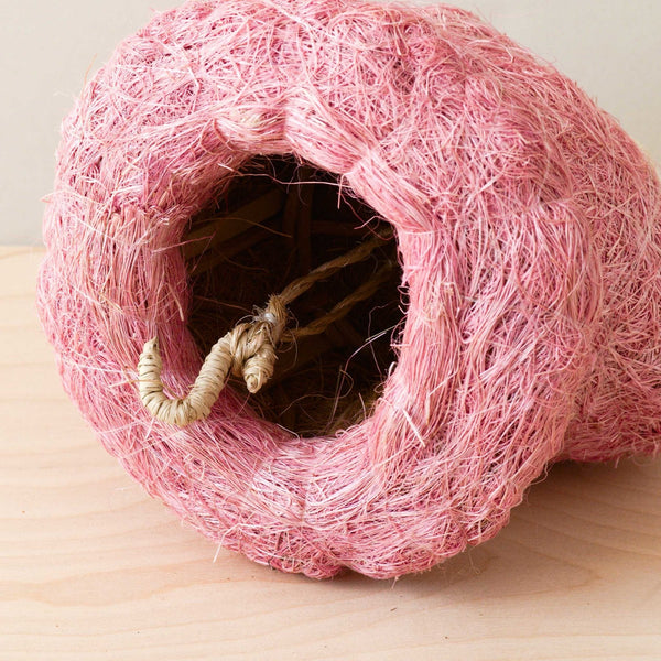 Pink woven cat house on a wooden surface