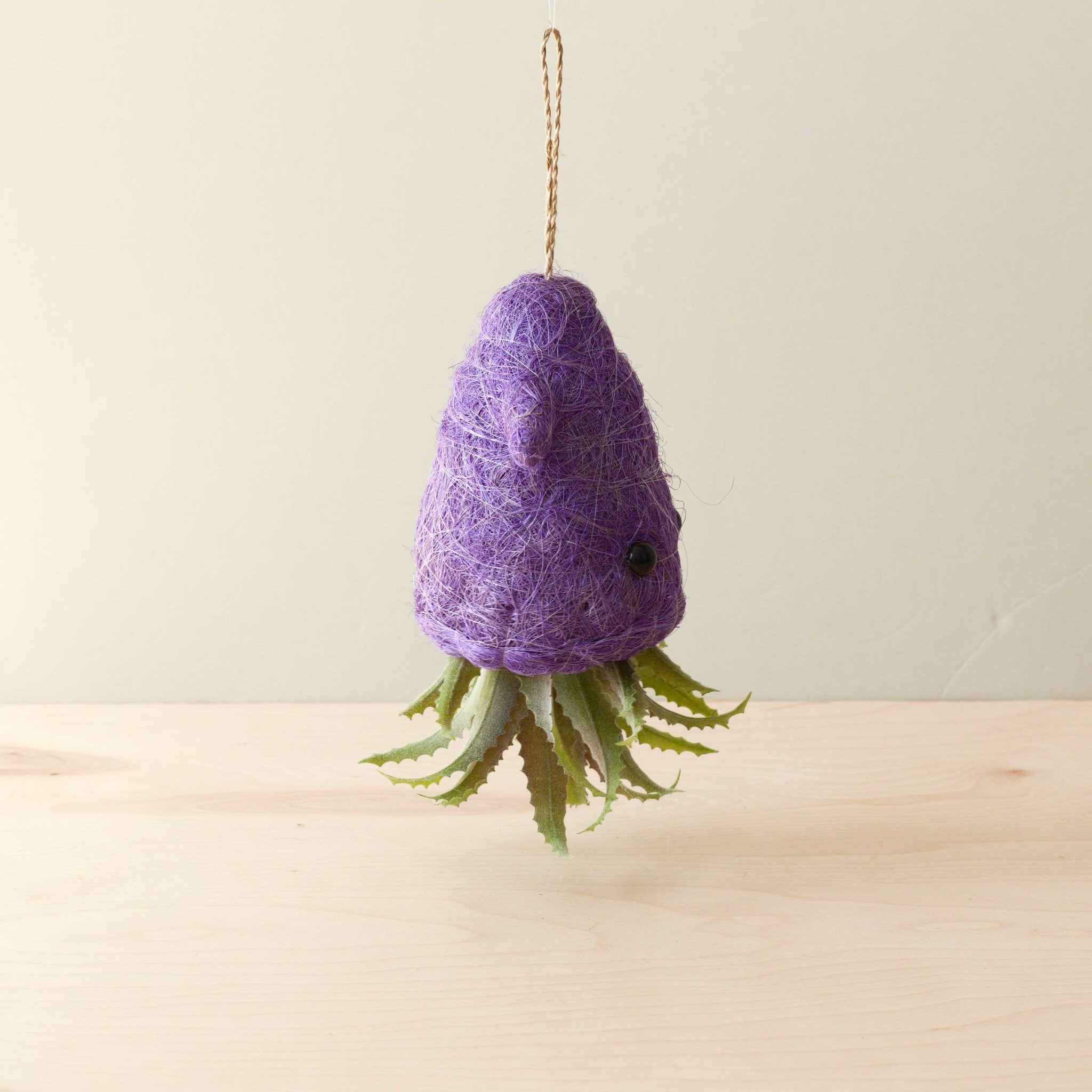 Purple felted octopus ornament hanging on a beige background